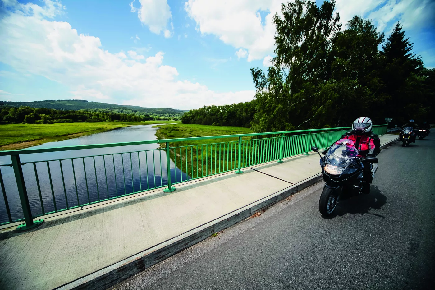 Motorräder auf einer grünen Stahlbrücke über einen Fluss