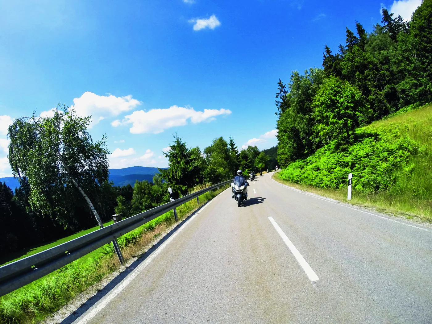 Motorrad auf einer Straße durch die bewaldete Hügellandschaft