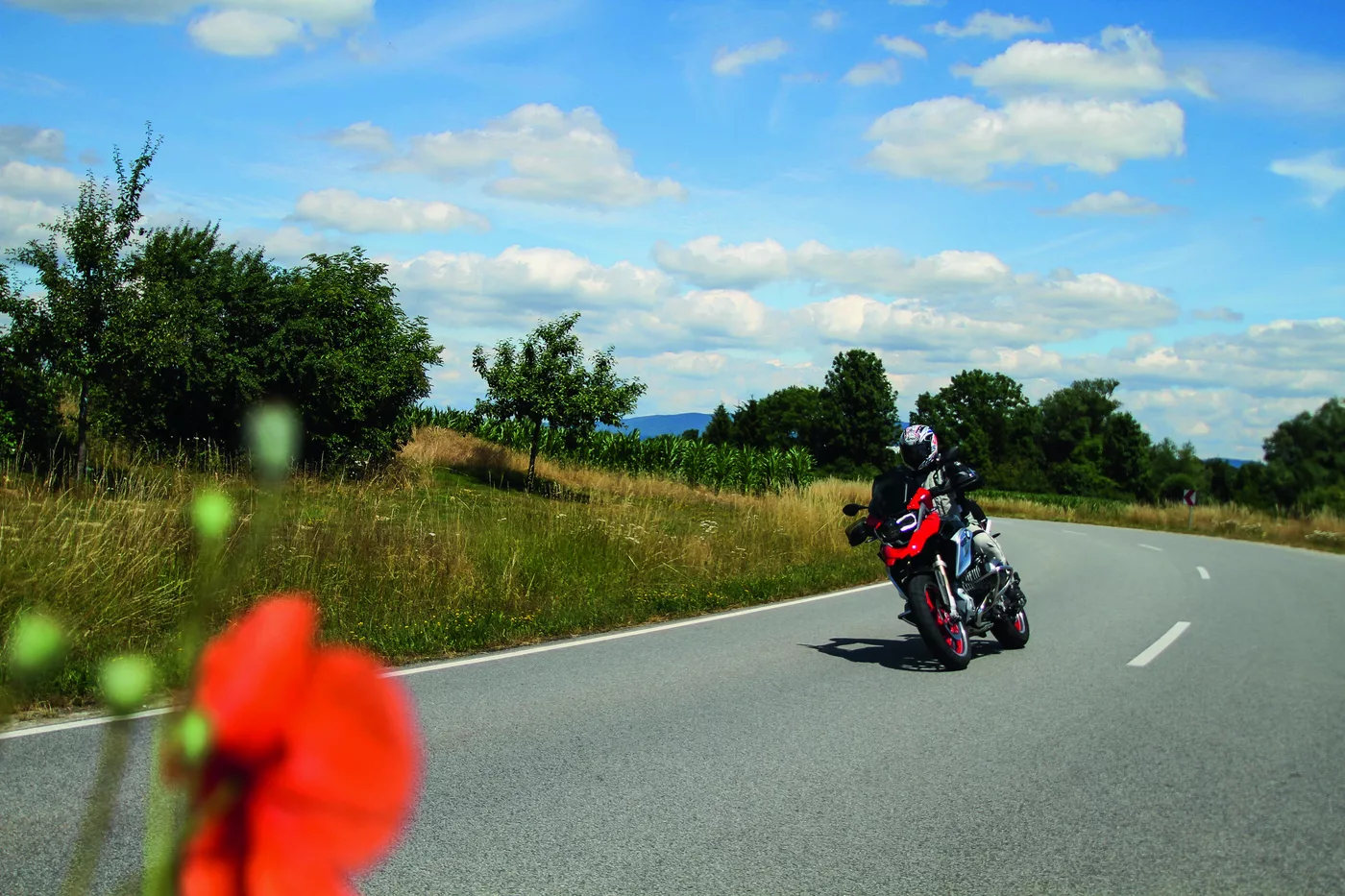Motorrad auf einer Landstraße, im Vordergrund eine rote Mohnblüte Motorrad auf einer Landstraße, im Vordergrund eine rote Mohnblüte